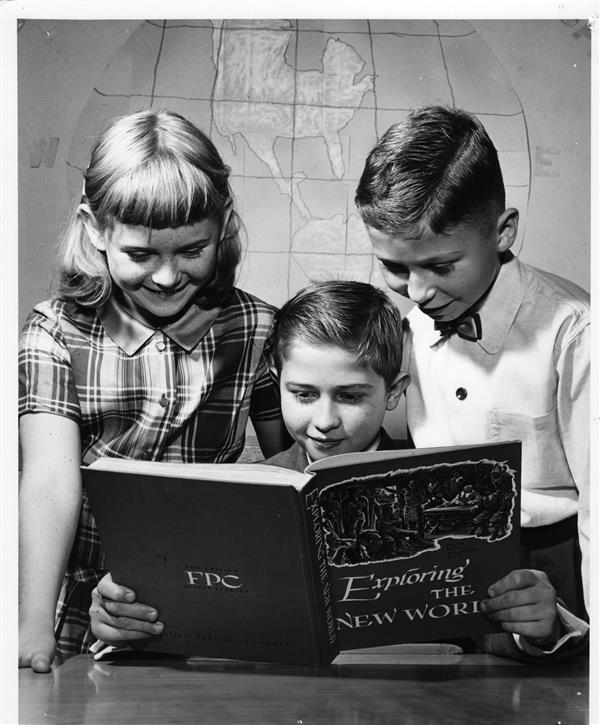 Black and white photo of three students examining a book.